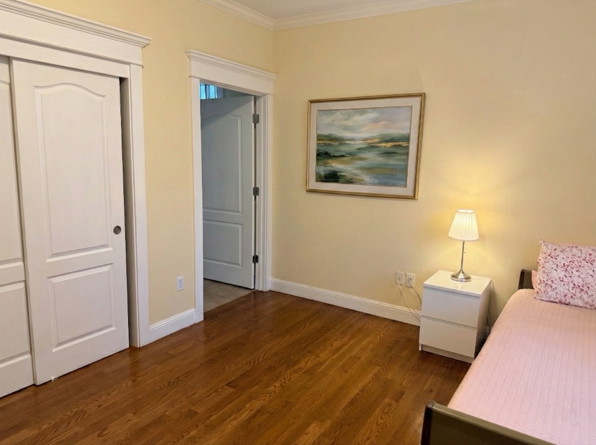 Cozy bedroom with landscape painting, bedside lamp, closet, and warm hardwood floors